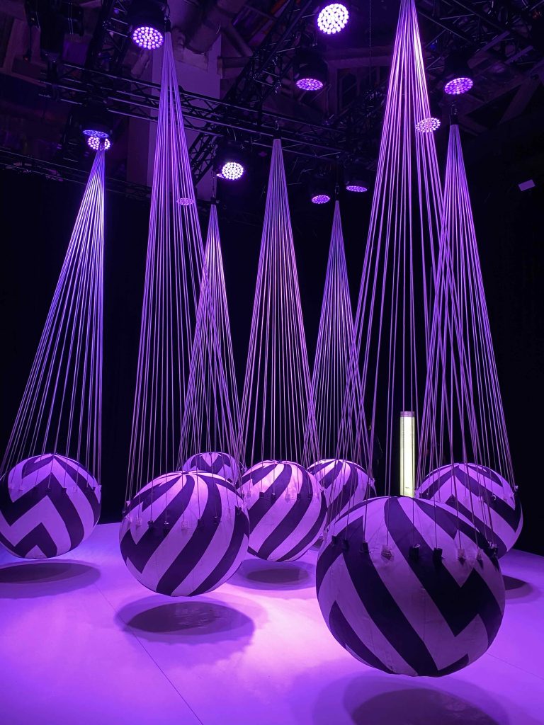 This is titled SWING; some balloons hung from the ceiling. When visitor walks in-between spheres, they move, showing interactive movements. Visitors trust the gentle movements replicating action and reaction, like in life